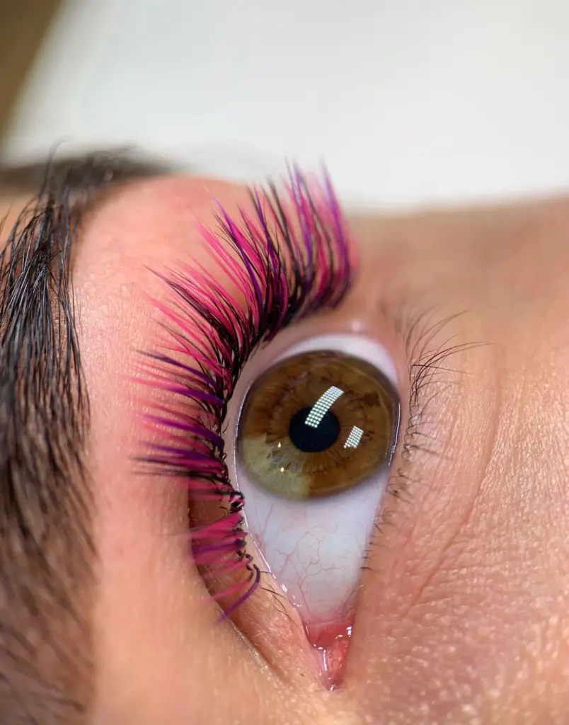 Közeli felvétel barna szemről, hosszú fekete, pink és lila szempillákkal.