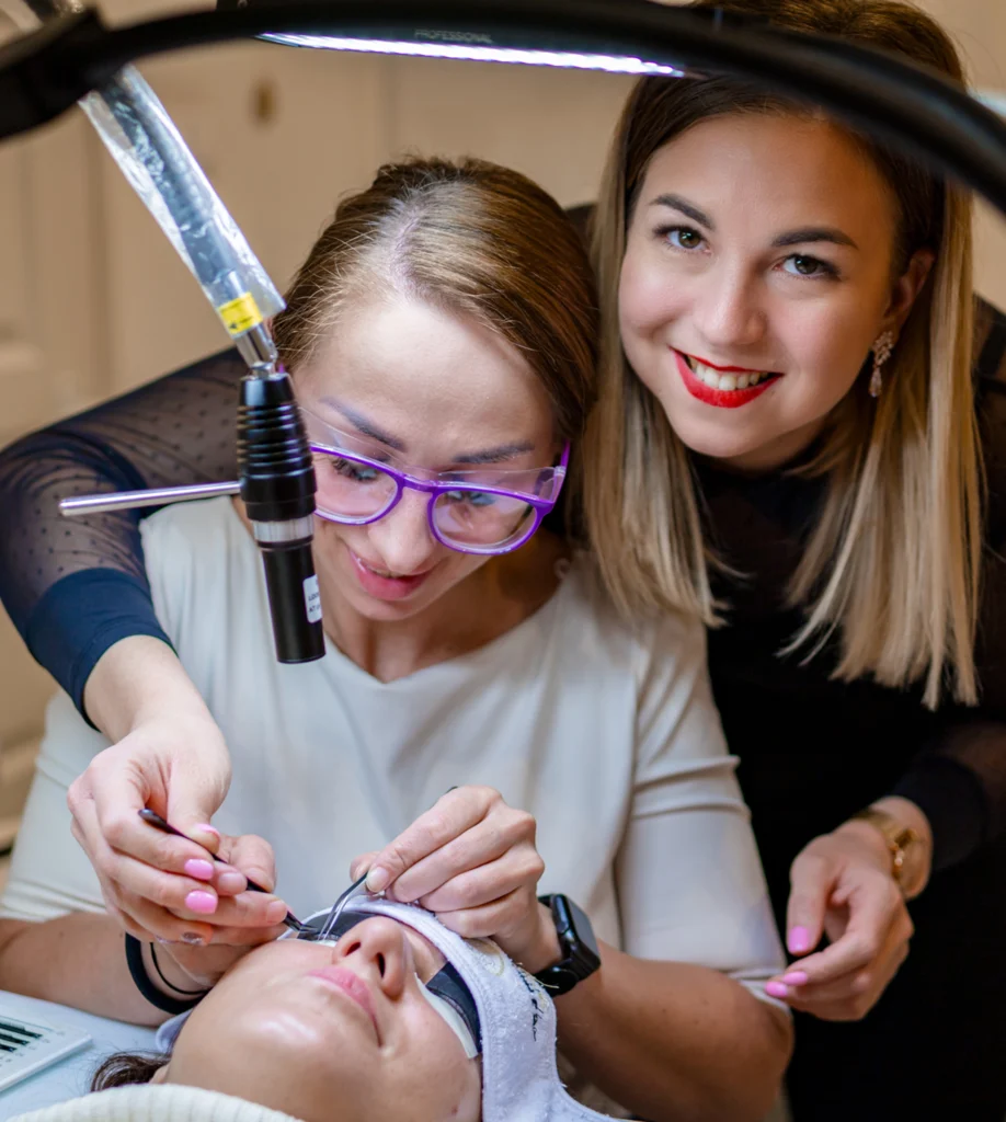 Egy oktató UV-LED lámpánál mutatja a szempillaépítést egy fekvő modellen.