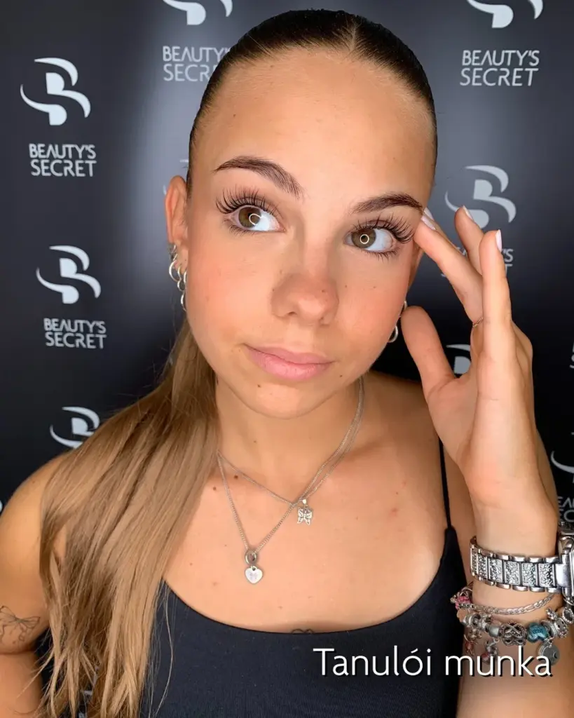 Hosszú, ívelt szempillákat viselő nő a Beauty’s Secret logós háttér előtt; felirat: „Tanulói munka”.