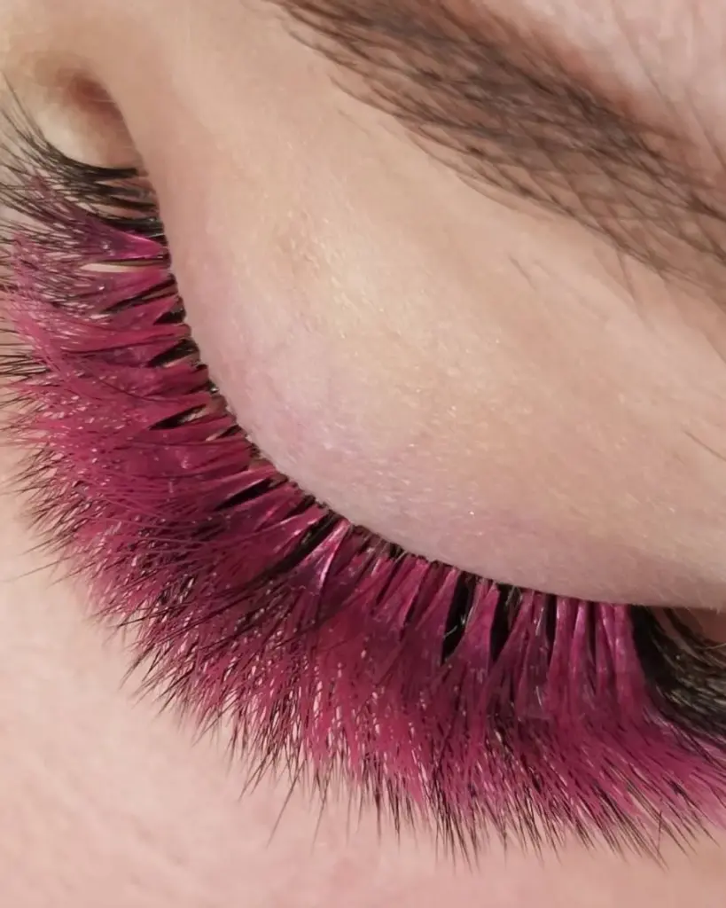 Közeli felvétel egy csukott szemről, élénk magenta szempilla-hosszabbítással.